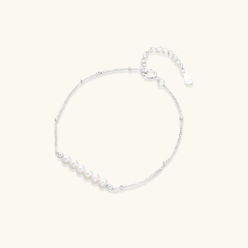 Delicate rhodium-plated silver chain bracelet with row of small baroque pearls centered on white background.
