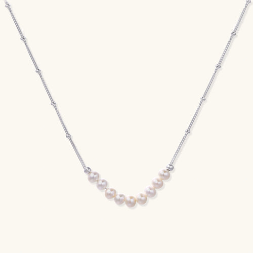 Delicate sterling silver chain necklace with small freshwater pearls arranged in a curved smile arc on cream background.