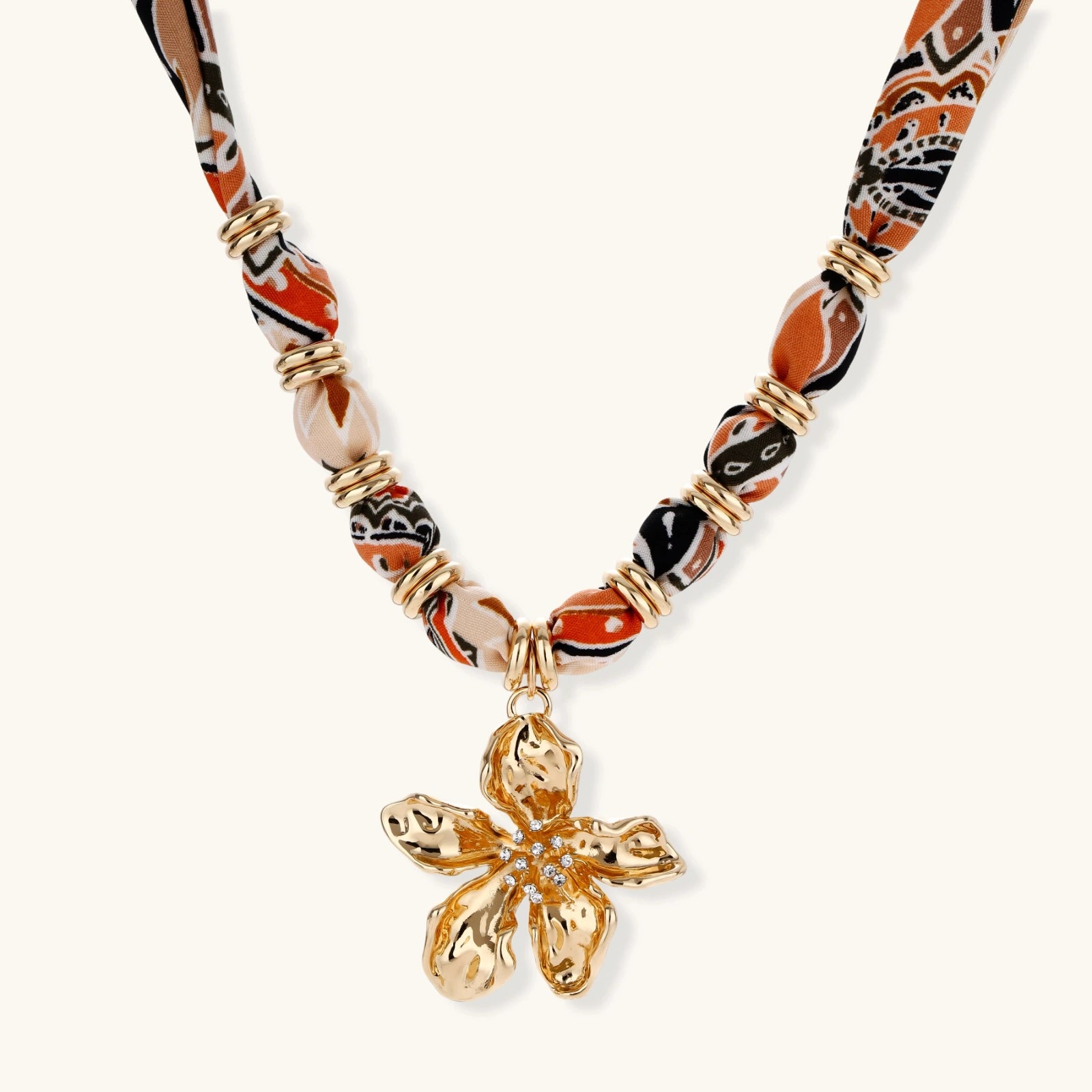 Vibrant patterned fabric necklace with gold-toned flower pendant featuring rhinestone center on white background