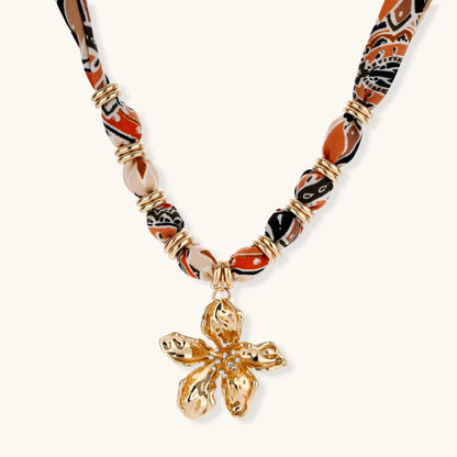 Vibrant patterned fabric necklace with gold-toned flower pendant featuring rhinestone center on white background
