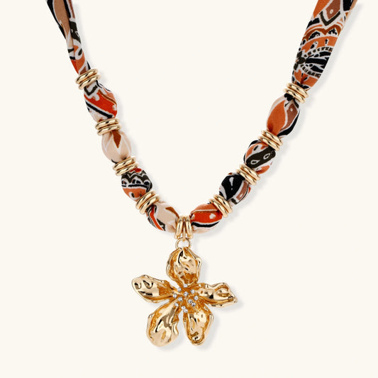 Vibrant patterned fabric necklace with gold-toned flower pendant featuring rhinestone center on white background