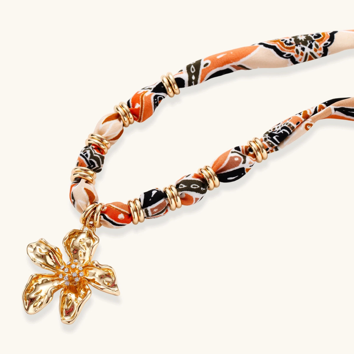 Vibrant patterned fabric necklace with gold-toned flower pendant featuring rhinestone center on white background