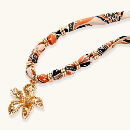 Vibrant patterned fabric necklace with gold-toned flower pendant featuring rhinestone center on white background