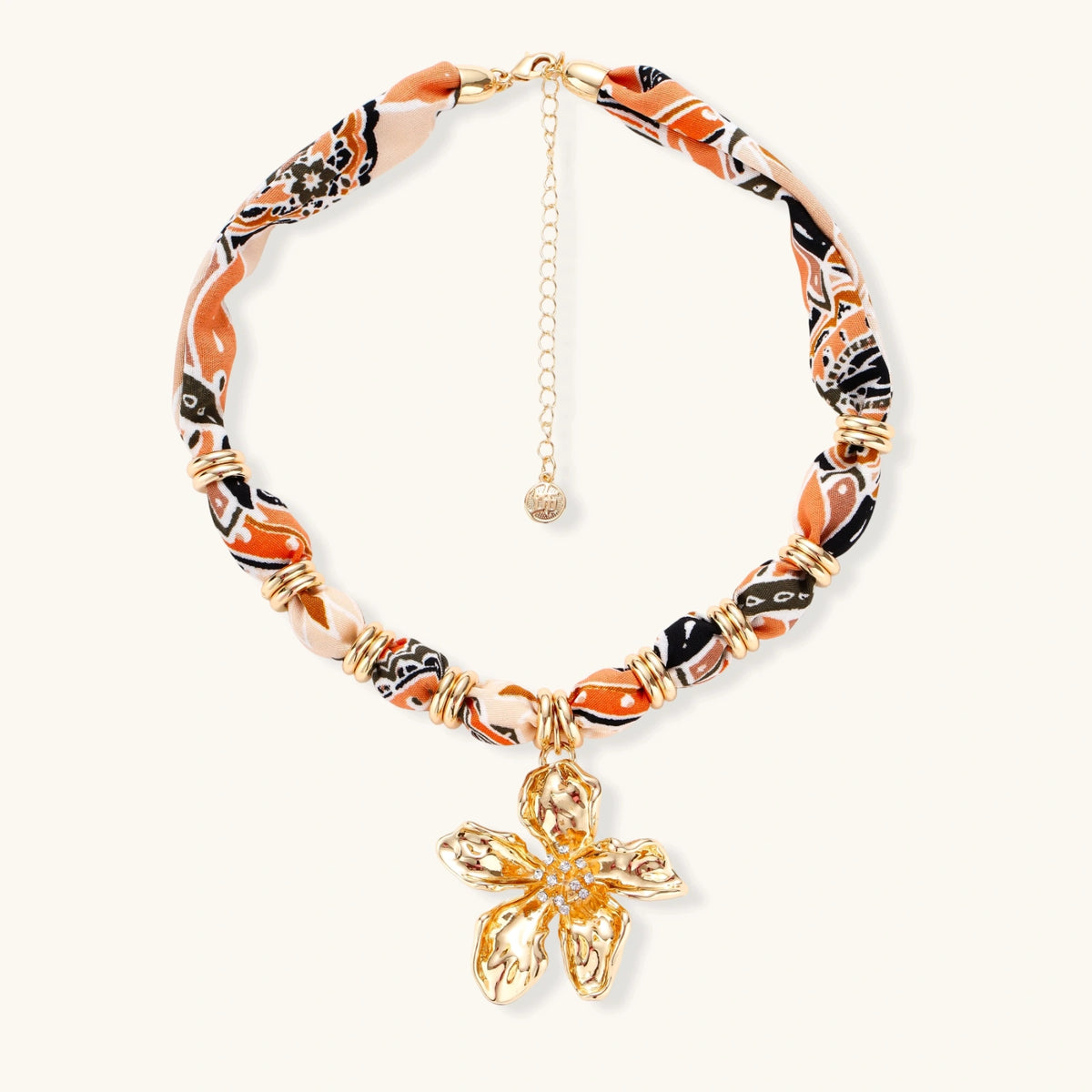 Vibrant patterned fabric necklace with gold-toned flower pendant featuring rhinestone center on white background