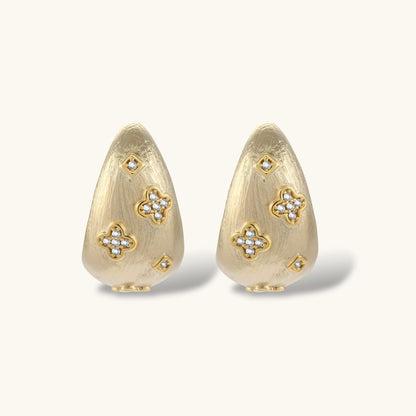 Curved gold-plated hoop earrings with four-leaf clover and diamond-shaped crystal details on white background